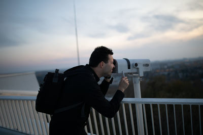 Side view of man looking through telescope against sky