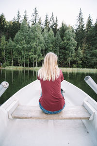 Rear view of woman sitting on lake against trees
