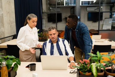 Group of multiethnic coworkers discussing business project together while surfing on netbook at table in light modern office