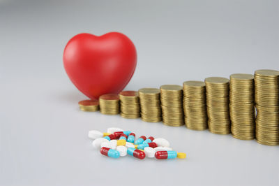 Close-up of coins by pills and heart shape stress ball on white background
