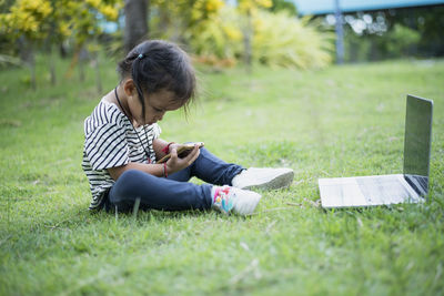 Side view of woman using digital tablet while sitting on field