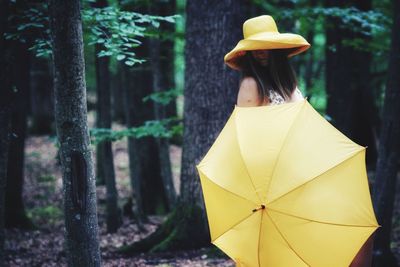 Woman holding umbrella while standing in forest
