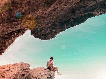 Full length of shirtless man standing on rock by sea