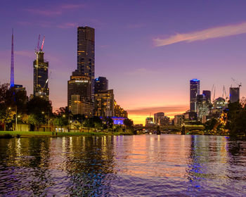 River by illuminated buildings against sky in city