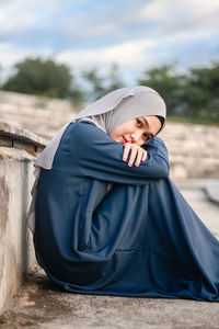 Young woman sitting against wall