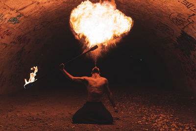 Rear view of shirtless man standing by fire at night