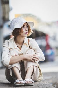 Full length of woman looking away while sitting outdoors