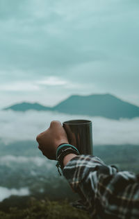 Hand of hiker holding mug against sky