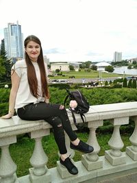 Portrait of young woman sitting against building in city