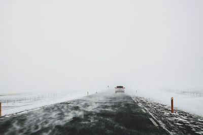 Road by frozen lake against clear sky during winter