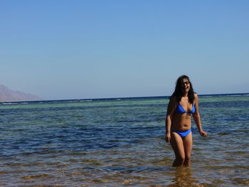 Full length of young woman standing in sea against clear sky