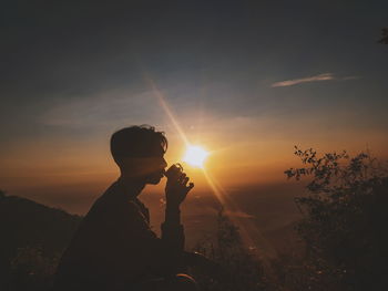 Silhouette man drinking coffee against sky during sunset