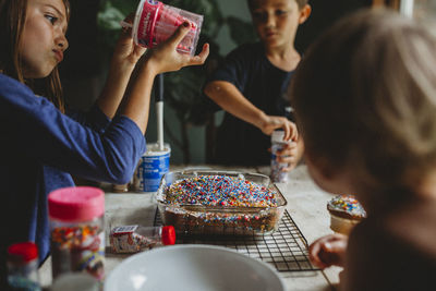 Siblings decorating cake with overabundance of colorful sprinkles