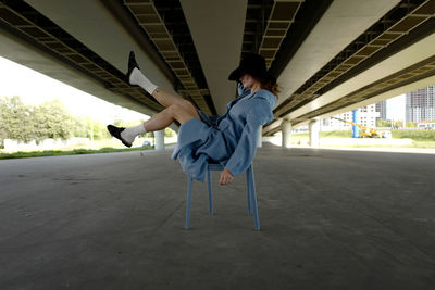 Full length of woman sitting on chair under bridge