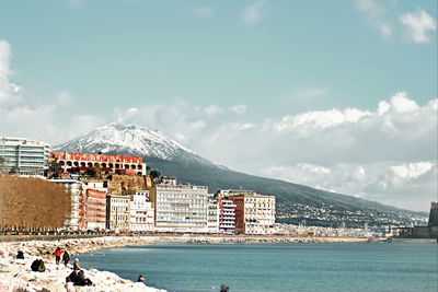 Buildings by sea against cloudy sky