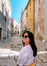 Young woman from behind, walking in city, looking back, old town, happy, smiling.