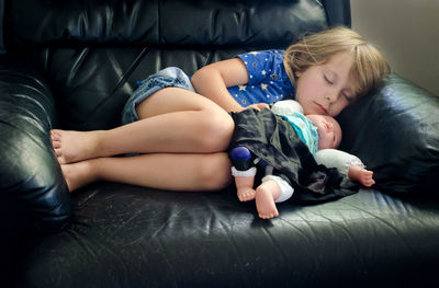 Tired little girl with her favorite doll falls asleep in grandpa's big leather chair
