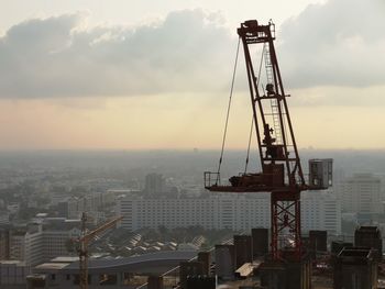 Crane by buildings against sky during sunset