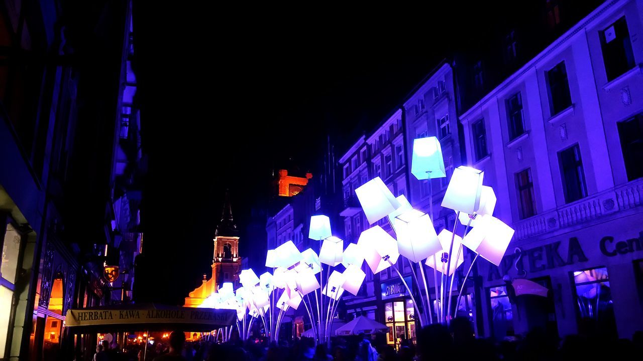 illuminated, night, built structure, architecture, building exterior, large group of people, lighting equipment, city, blue, low angle view, light - natural phenomenon, clear sky, city life, building, dark, modern, multi colored, crowd, outdoors