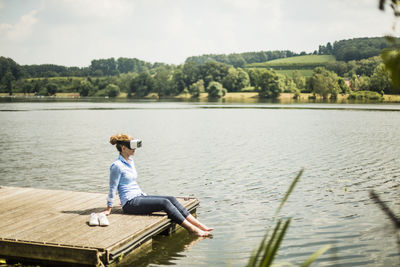 Man sitting by lake against sky