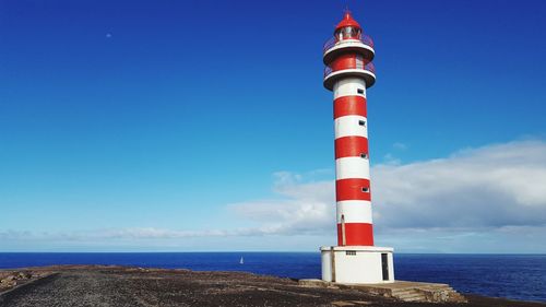 Lighthouse by sea against blue sky