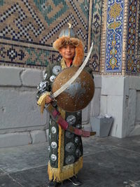 Young man wearing costume holding sword standing against wall