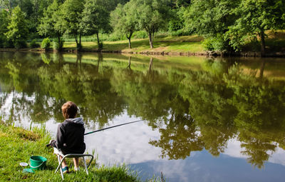 Boy fishing in lake against trees