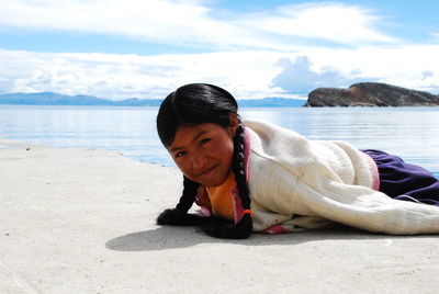 Portrait of mid adult woman lying on sand at beach against cloudy sky