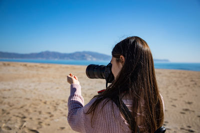 Beautiful woman taking a picture of a sea shell holding it with her hand close back shot at beach