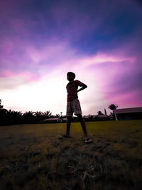 Low angle view of girl standing on field against sky during sunset