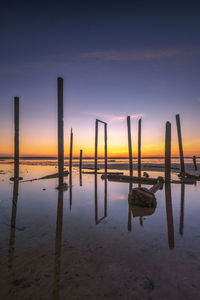 Wooden posts on beach against sky during sunset