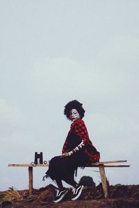 Full length of young woman sitting on snow against sky