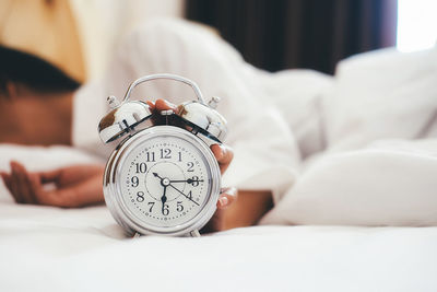 Close-up of alarm clock and woman on bed