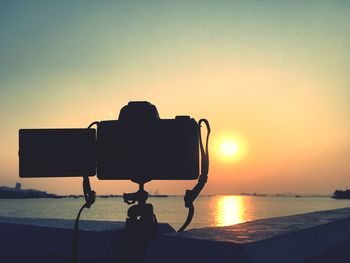 Silhouette photographing by sea against sky during sunset