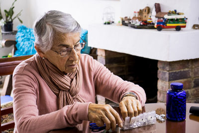 Senior woman taking medicine while sitting by table at home