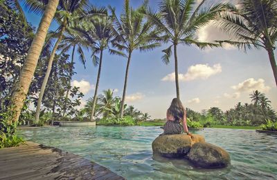 Rear view of woman sitting on rock in pool