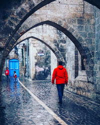 Rear view of people walking on wet road amidst buildings