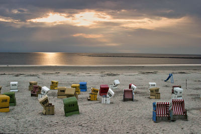 Hooded chairs at beach against sky during sunset