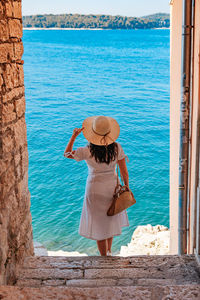 Young woman from behind. woman in white dress standing on stone stairs by sea.