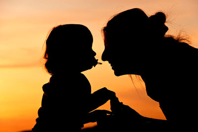 Silhouette of girl playing with mother against sky during sunset