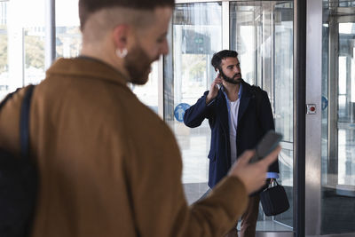 Businessman talking on mobile phone while standing with coworker in background against building