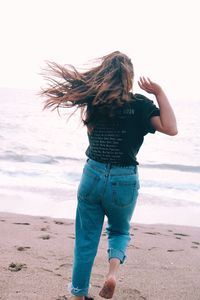 Rear view of woman running on sand towards sea at beach