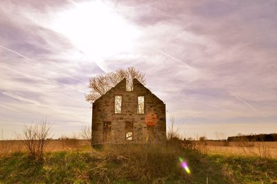 Abandoned house on grassy field against cloudy sky