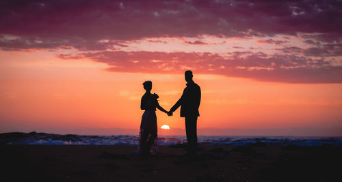 Silhouette friends standing on shore against orange sunset sky