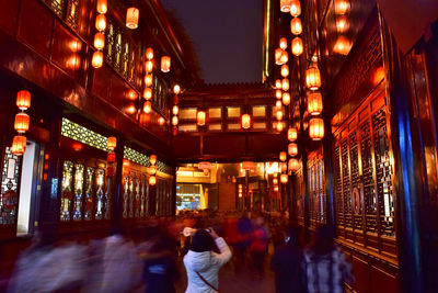 People walking on illuminated street amidst buildings at night