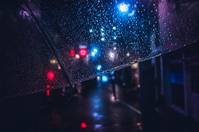 Illuminated city seen through wet window during rainy season