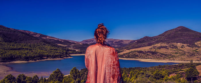 Rear view of woman standing on mountain against clear blue sky