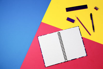 High angle view of spiral notebook with school supplies on colored background