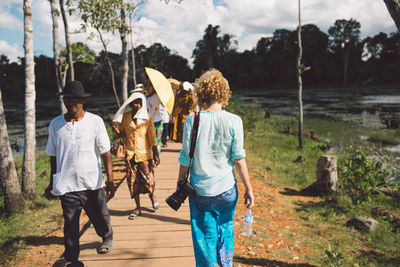 Rear view of people walking on shore against trees