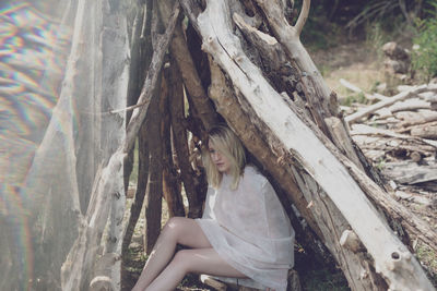 Woman sitting by tree trunk in forest